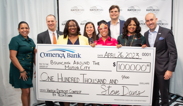 Cathryn Coleman, founder and owner of Bouncing Around the Motor City, holds a large check for $100,000 with representatives from TechTown and Comerica Bank