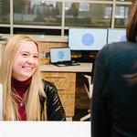 A woman sitting behind a front desk smiles at another person