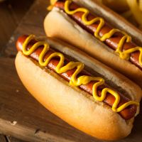 Two hot dogs in hot dog buns with yellow mustard drizzled on top of both