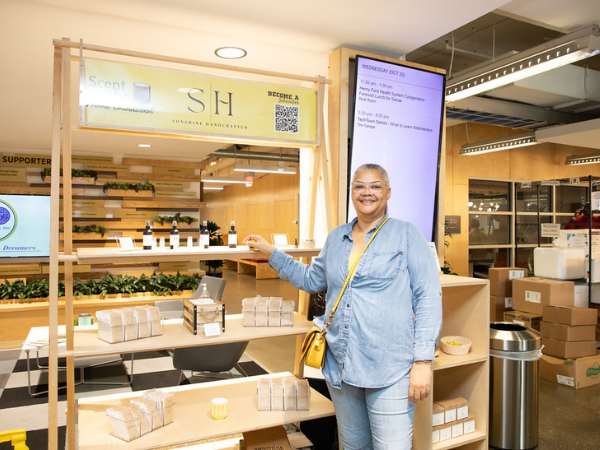 A person smiles in front of the vendor display for their business Sunshine Handcrafted