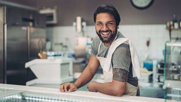 A person wearing an apron with a towel over their shoulder smiles for a photo